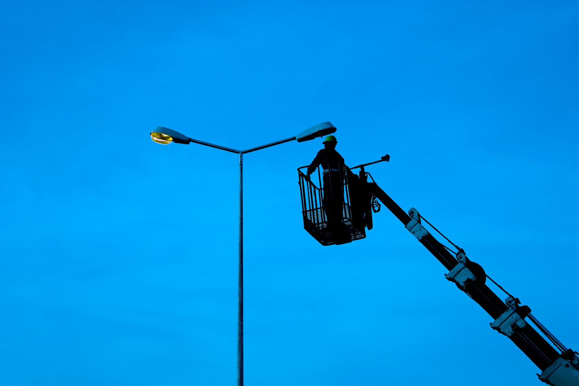 Montør i lift arbeider på et gatelys mot blå himmel